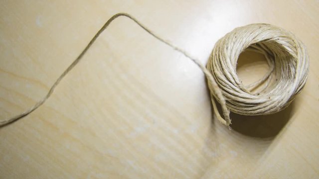 Stop motion of a ball of string unrolling untill it end, on a light wooden background