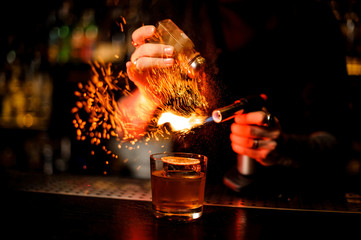 Professional bartender adding to a cocktail brown spice and flame it