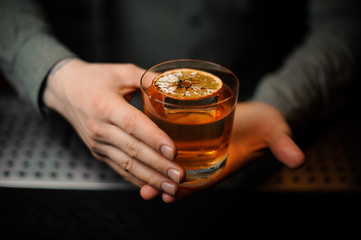 Bartender serving a delicious brown cocktail with a dried orange