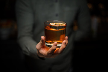 Male bartender serving a delicious brown cocktail with a dried orange on the one hand