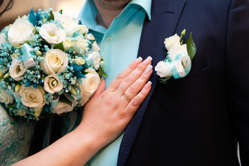 Wedding boutonniere on suit of groom and the hand of bride 