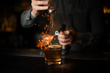 Bartender adding to a cocktail cinnamon and flaming it