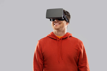 3d technology, virtual reality, entertainment and people concept - happy young man in vr glasses playing game over grey background