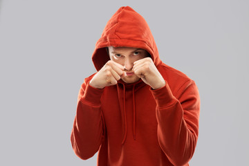 combat, aggression and people concept - young man in red hoodie fighting with fists or boxing over...