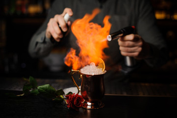 Professional bartender spraying on the cocktail in the golden cup and flaming it