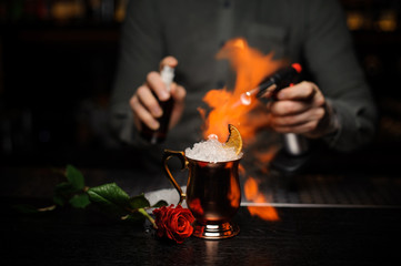 Bartender spraying on the cocktail in the golden cup and flaming it with a burner