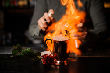 Bartender spraying on the delicious cocktail in the golden cup and flaming it with a burner