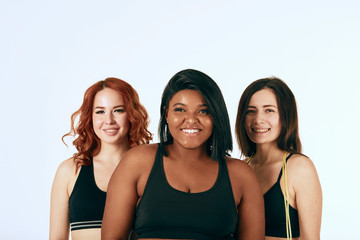 African happy overweight woman in company of two caucasian slim girlfriends, dressed in sportive clothes . Fitness, sport, diet concept.