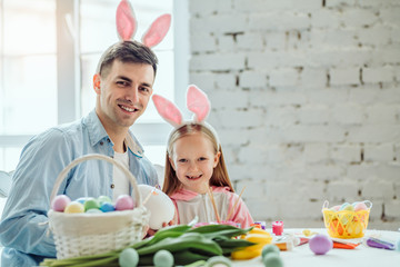 My dad is the best in the world!Father and daughter are preparing for Easter together.On the table is a basket with Easter eggs, flowers and paint.