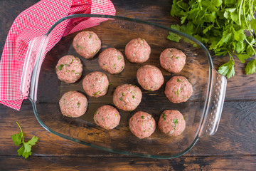 Uncooked raw meatballs with mozzarella in baking glass dish on wooden rustic table, top view