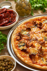 Pizza with mushrooms, cheese, basil leaves on an aluminum pizza pan. Fresh arugula, olives, dry tomatos and capers