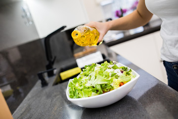 healthy eating, vegetarian food, dieting and people concept - close up of young woman dressing vegetable salad with olive oil at home