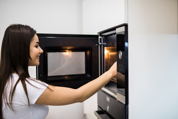 Fototapeta na wymiar A young woman is opening the oven in her modern kitchen