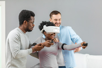 Happy African girl learning to use virtual reality gadget before buying it and her boyfriend...
