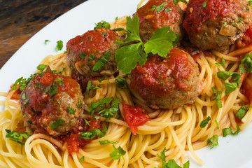 Pasta and meatballs with mozzarella, tomato sauce, fresh parsley on white plate, close-up