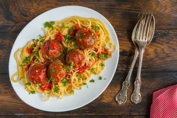Pasta and meatballs with mozzarella, tomato sauce, fresh parsley, white plate on wooden rustic table, top view