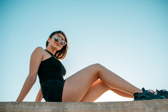 Young beautiful girl in black shorts and top posing on the roof at sunset