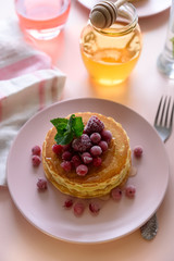 Stack of pancakes with frozen raspberry, red currant and honey on pink background. Selective focus