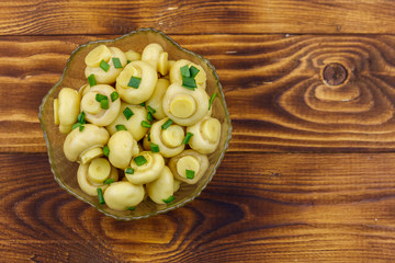 Glass bowl with pickled champignons. Marinated mushrooms on wooden table