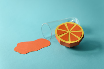 Spilled juice and paper orange fruit on blue background. Copy space. Creative or art food concept