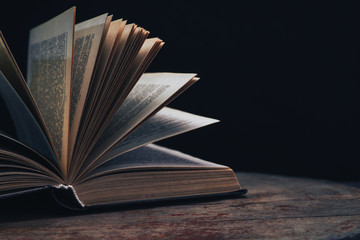One open old book on a round wooden table. Beautiful dark background...