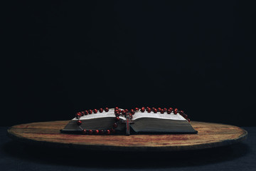 Bible and the crucifix beads on a old round table. Beautiful night background. Religion concept...