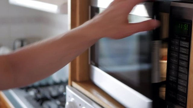 Man places leftover meal in a white bowl into a microwave oven and sets the timer. He then closes the door and starts the appliance.