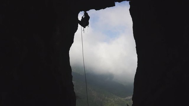 Climber silhouette descending the rock by rope at sky background