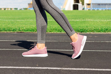 Girl legs in pink sport shoes standing on a running track with stadium stands. Sports and healthy concept