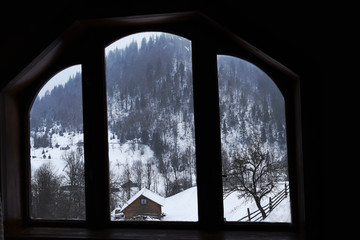 window in the countryside with a view of the rural house and a mountainous winter landscape outside the window.