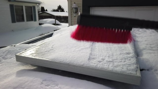 Someone brushing snow off of a solar panel that is mounted on top of an SUV at half speed