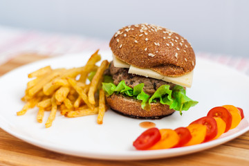 Hamburger with vegetables and french fries on a white plate