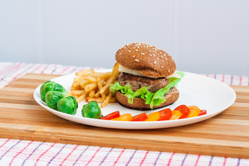 Hamburger with vegetables and french fries on a white plate