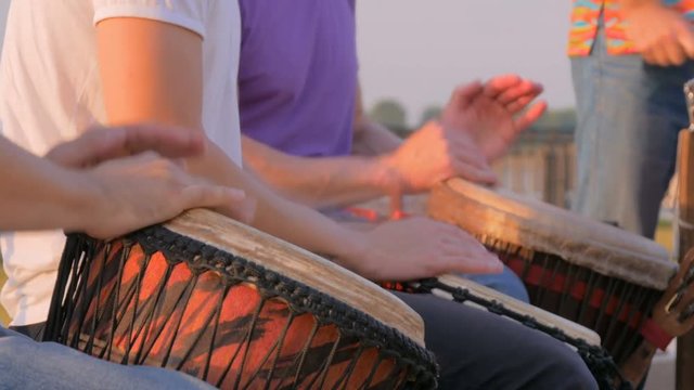 Unrecognizable group of people playing ethnic percussion drum musical instruments on street - close up shot. Street music and urban culture concept