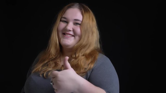 Closeup shoot of young overweight caucasian female showing a thumb up and smiling happily while looking straight at camera