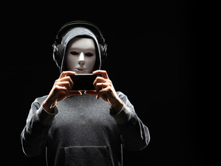 Computer hacker in white mask and hoodie. Obscured dark face. Data thief, internet fraud, darknet and cyber security concept.