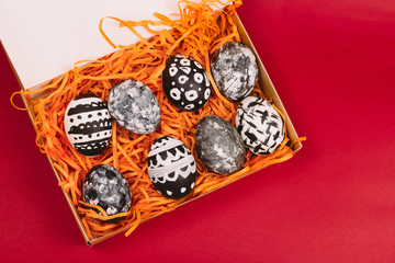 top view collection of dyed black and white easter eggs in box on a red background
