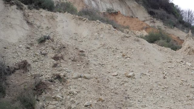 Close-up tilt up over a huge pile of dirt blocking passage through a mountainside road after a landslide