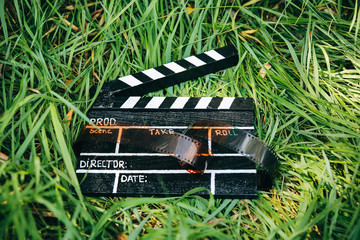 Black clapperboard with film lying on the grass in the nature outdoors. Directing and of amateur...