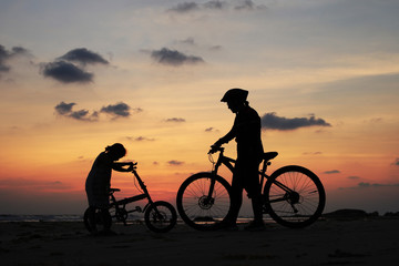 Silhouette of stepmother alone with children and bicycle at sunset background