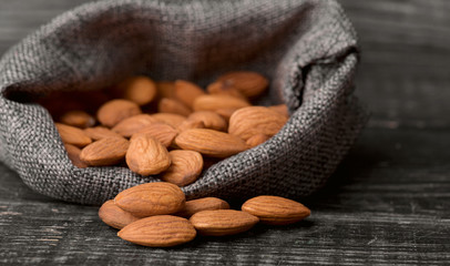 Almonds in gray bag on textured  dark wooden background, top view. Copy space.