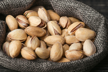 Roasted pistachios  in gray bag on textured  dark wooden background, top view. Copy space. 