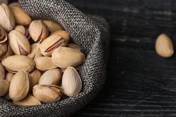 Roasted pistachios  in gray bag on textured  dark wooden background, top view. Copy space. 