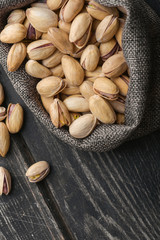 Roasted pistachios  in gray bag on textured  dark wooden background, top view. Copy space. 