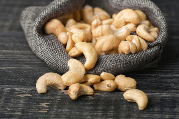 Cashew nuts in gray bag on textured  dark wooden background, top view. Copy space. 