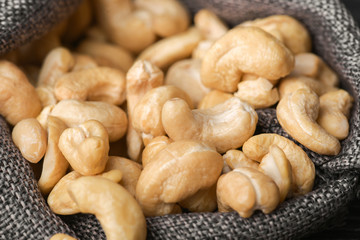 Cashew nuts in gray bag on textured  dark wooden background, top view. Copy space. 