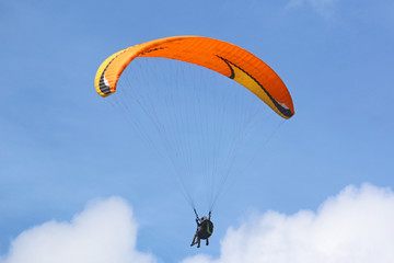 Tandem paraglider flying orange wing