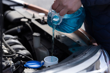 Man is holding bottle of blue antifreeze in hands and pouring antifreeze liquid for washing car...