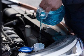 Man is holding bottle of blue antifreeze in hands and pouring antifreeze liquid for washing car screen