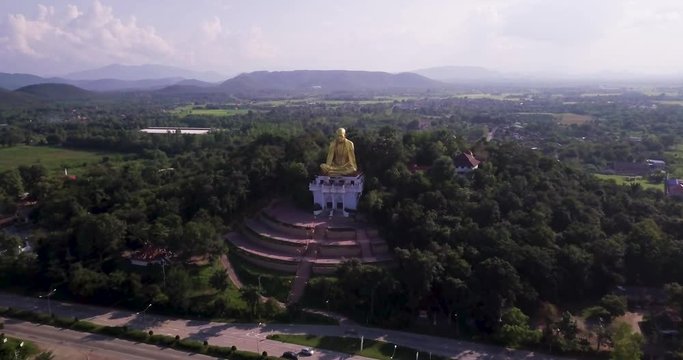 Aerial shot of a huge golden buddha statue next to a very busy highway in Lamphun, Thailand.